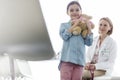 Portrait of smiling girl holding teddybear while doctor sitting at hospital