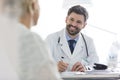 Smiling doctor discussing with mature patient while writing prescription at desk in hospital Royalty Free Stock Photo