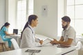 Medical clinic. Smiling woman doctor sitting and listening to talking man patient during consultation