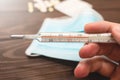 A medical clinical mercury thermometer in person`s hand showing the temperature of 39 C. High temperature. wooden background.