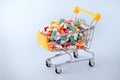 Medical colourful pills and capsules in shopping small trolley on light blue background.Mini cart filled to the top with drugs.