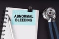 On a black surface, a stethoscope, a notebook, a pen and a blue sticker with the inscription - ABNORMAL BLEEDING Royalty Free Stock Photo