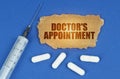 On a blue surface lie a syringe, pills and a cardboard sign with the inscription - Doctors Appointment