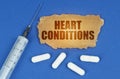 On a blue surface lie a syringe, pills and a cardboard sign with the inscription - HEART CONDITIONS