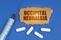 On a blue surface lie a syringe, pills and a cardboard sign with the inscription - Occipital Neuralgia