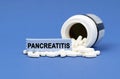 On a blue surface lies a jar of pills and a sign with the inscription - PANCREATITIS