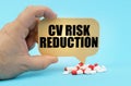 On a blue surface are pills in a persons hand, a sign with the inscription - CV Risk Reduction