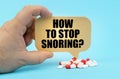 On a blue surface are pills in a persons hand, a sign with the inscription - HOW TO STOP SNORING