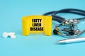 On a blue surface, a stethoscope, pills, a pen and a yellow sign with the inscription - Fatty liver disease