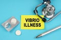 On a blue surface, a stethoscope, pills, a pen and a yellow sticker with the inscription - Vibrio illness
