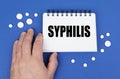 On the blue surface of the tablet, a hand and a notepad with the inscription - SYPHILIS