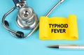 On the blue surface there is a stethoscope, a pen and a yellow sticker with the inscription - Typhoid fever