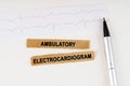 On the cardiogram lies a pen and torn paper with the text - Ambulatory Electrocardiogram