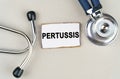 On a gray background, a stethoscope and a cardboard sign with the inscription - Pertussis