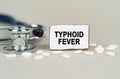 On a gray background, a stethoscope, pills and a cardboard plate with the inscription - Typhoid fever