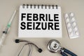 On a gray surface there is a syringe, a stethoscope and a notepad with the inscription - Febrile seizure Royalty Free Stock Photo