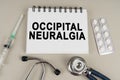 On a gray surface there is a syringe, a stethoscope and a notepad with the inscription - Occipital neuralgia