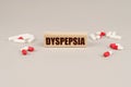 On a gray surface are tablets, capsules and a wooden plate with the inscription - Dyspepsia