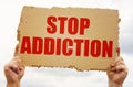 In the hands of a man is a cardboard sign with the inscription - Stop Addiction