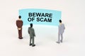 Miniature figures of people stand in front of a blue sign with the inscription - Beware of scam