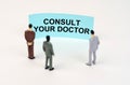 Miniature figures of people stand in front of a blue sign with the inscription - Consult your doctor Royalty Free Stock Photo