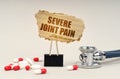 Near the stethoscope are pills and a clip with a cardboard sign - severe joint pain