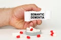 On a white background, medical capsules, in the hands of a person a paper plate with the inscription - Semantic dementia