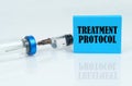 On a white reflective surface there is a syringe with an ampoule and a plate with the inscription - treatment protocol