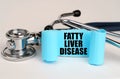 On a white surface lies a stethoscope and a blue roll of paper with the inscription - FATTY LIVER DISEASE