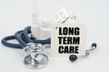 On a white surface, medicines, a stethoscope and writing paper with the text - LONG TERM CARE