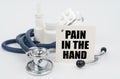 On a white surface, medicines, a stethoscope and writing paper with the text - pain in the hand