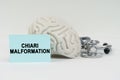 On a white surface next to the brain there is a stethoscope and stickers with the inscription - Chiari malformation Royalty Free Stock Photo