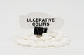 On a white surface are pills and torn paper with the inscription - ULCERATIVE COLITIS