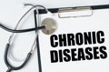 On a white surface, a stethoscope and a tablet with an inscription - CHRONIC DISEASES