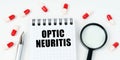 On a white surface are tablets, a pen, a magnifying glass and a notepad with the inscription - Optic neuritis