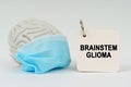 On a white surface there is a brain with a blue mask and a notepad with the inscription - Brainstem glioma