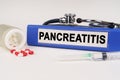 On a white surface there are pills, a syringe and a folder with the inscription - Pancreatitis