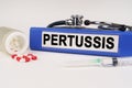 On a white surface there are pills, a syringe and a folder with the inscription - Pertussis