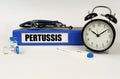 On a white surface, a thermometer, a stethoscope and a folder with the inscription - Pertussis