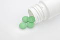 Medical conceptual photo. Green round pharmaceutical pills spilling out of a white pill bottle.