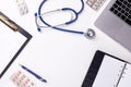 Medical desk with stethoscope, latptop, pills and blank paper on clipboard.