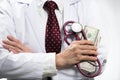 Medical doctor holding money and stethoscope in hospital setting Royalty Free Stock Photo