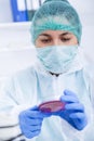 Medical doctor in protective gloves and surgical mask and hat comparing with liquid in laboratory. Royalty Free Stock Photo