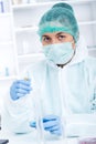 Medical doctor in protective gloves and surgical mask and hat comparing with liquid in laboratory. Royalty Free Stock Photo