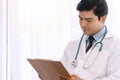 Doctor reading report document while sitting at his office. Handsome young guy wear uniform doctor holding clipboard with Royalty Free Stock Photo