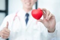 Medical doctor in white uniform holding red heart shape and showing thumbs up, medical concept