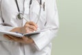 Medical doctor woman with stethoscope taking notes on her notepad against green background. Copy space