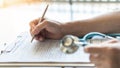 Medical doctor writing on patient personal health care record discharge form, or prescription paperwork in hospital Royalty Free Stock Photo