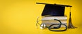 Medical education - college graduation cap with stethoscope and books on yellow background with copy space Royalty Free Stock Photo