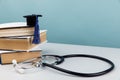 Medical education and healthcare theme. Stethoscope and graduation cap on stack of books on blue background Royalty Free Stock Photo